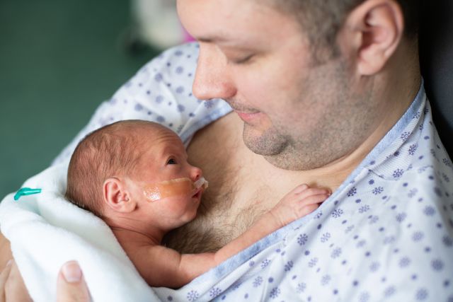 an infant child rests on the chest of a male caretaker