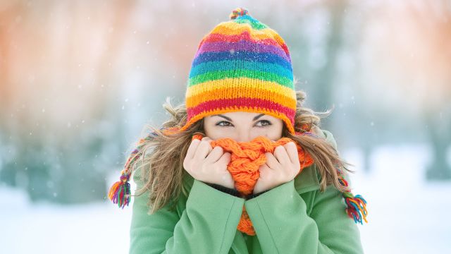 Young woman standing in snow with scarf around face.