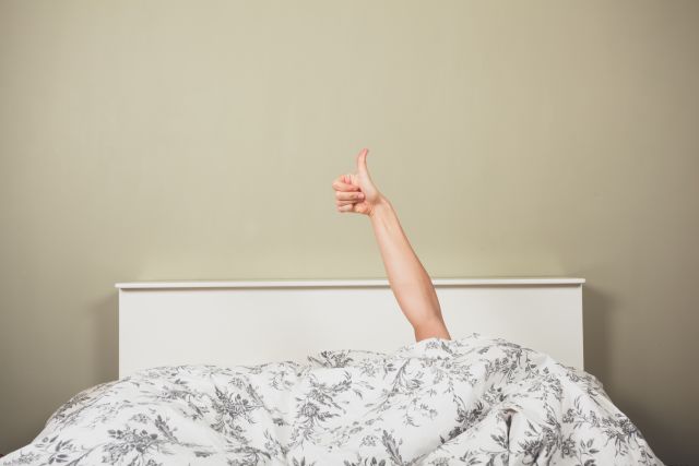 a person holds up a thumbs up sign from beneath a bedspread