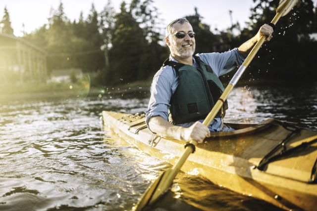 a middle aged man paddles a kayak across a lake