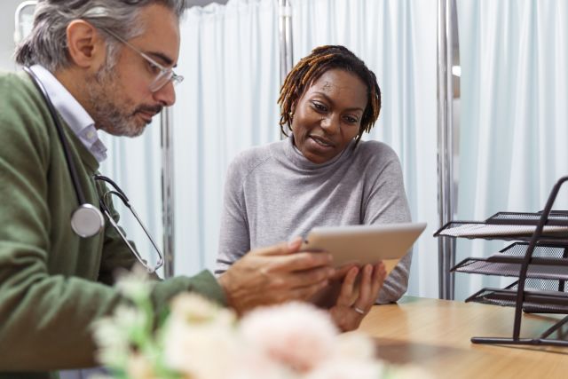 a middle-aged Black woman patient consults with her male Middle-Eastern doctor 