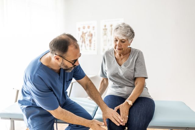 An older white woman has her knee examined by a healthcare provider