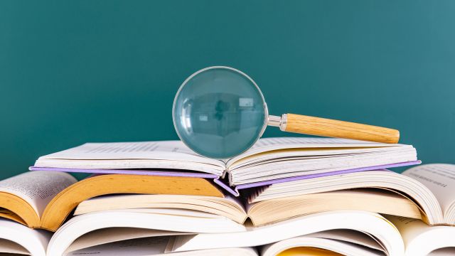 A magnifying glass rests on top of a pile of open books. Understanding the terminology around a health condition can be useful for patients and caregivers.