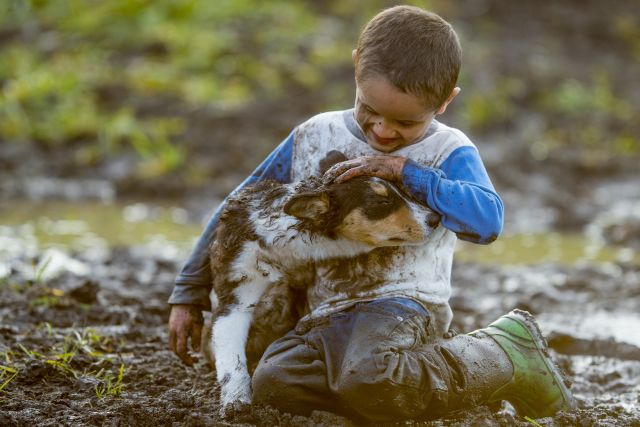 An elementary age boy is playing outside in the mud with his pet puppy. The little boy and the dog are covered in mud.