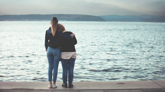 Adult daughter and mother with alzheimer's embracing while looking out over water