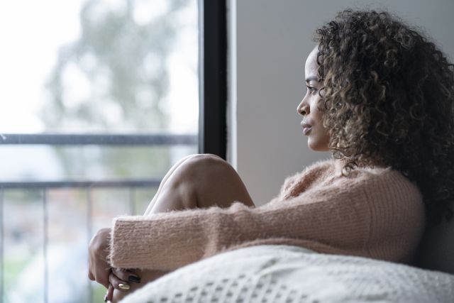 Black woman with bipolar disorder sitting in the living room of her home looking out of the window