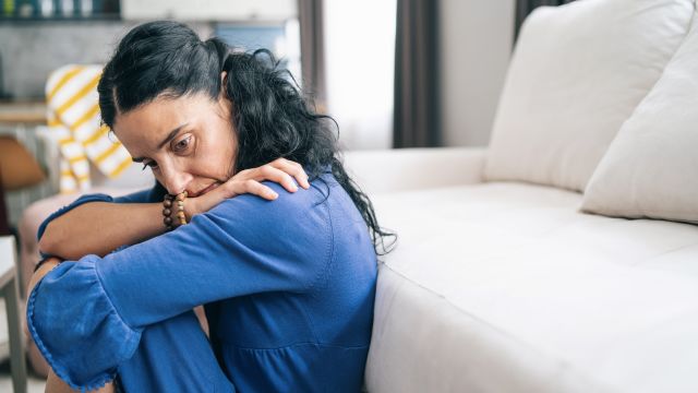 profile view of woman with depression leaning on her couch, hugging herself