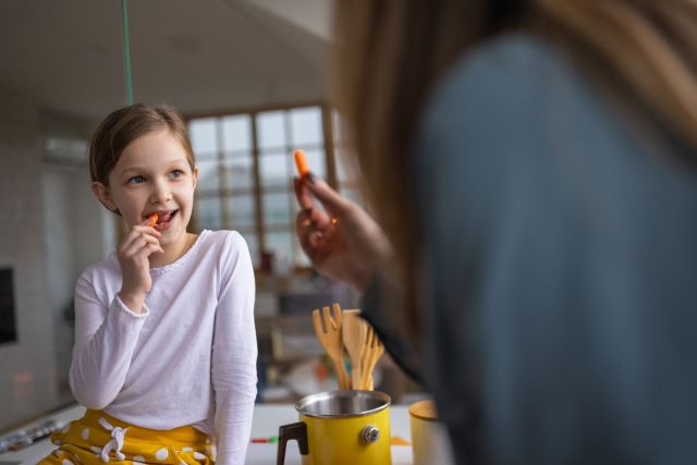 view of a young girl facing her mother, enjoying a snack of carrot sticks together