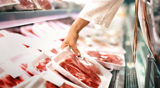 side view of woman inspecting a pack of steaks in the meat aisle of a grocery store