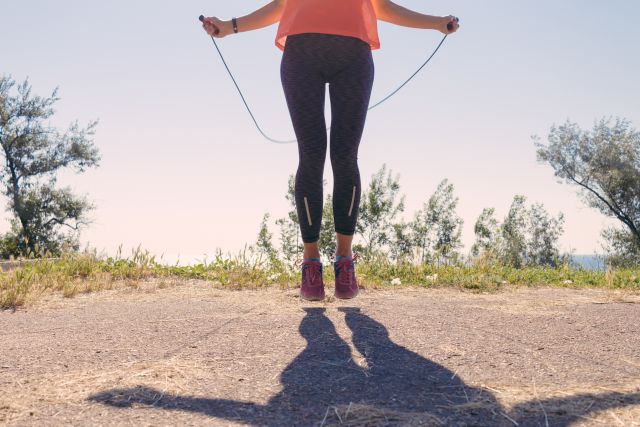 Girl in sportswear and sneakers jumping with a skipping rope