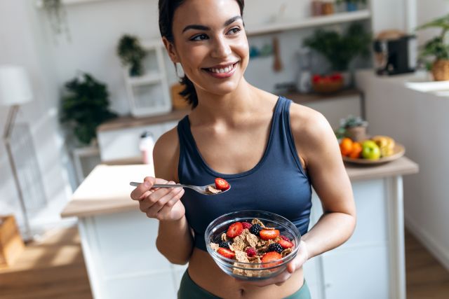 athletic young woman eating high-fiber cereal with berries