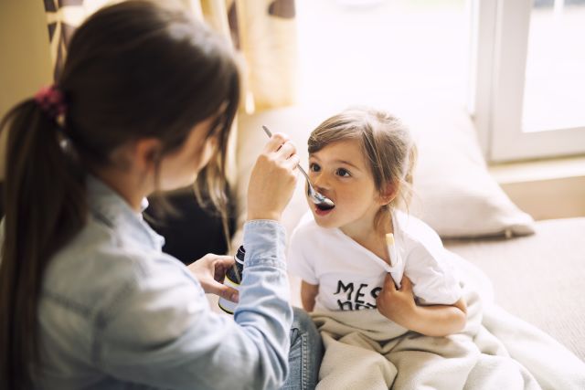 mother giving young daughter a spoonful of liquid medication