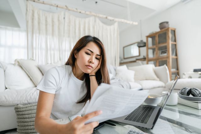 Stressed and worried young Asian woman looking at financial paperwork at home