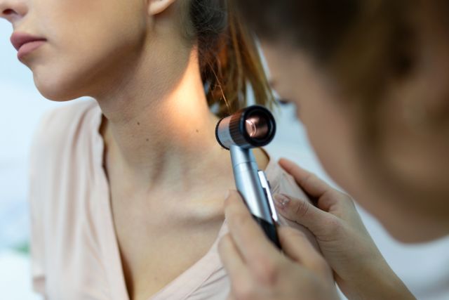 Dermatologist uses a dermatoscope to look at the mole on a woman's neck