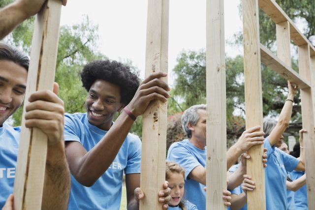 Group of volunteers propping up a wooden frame to build a house