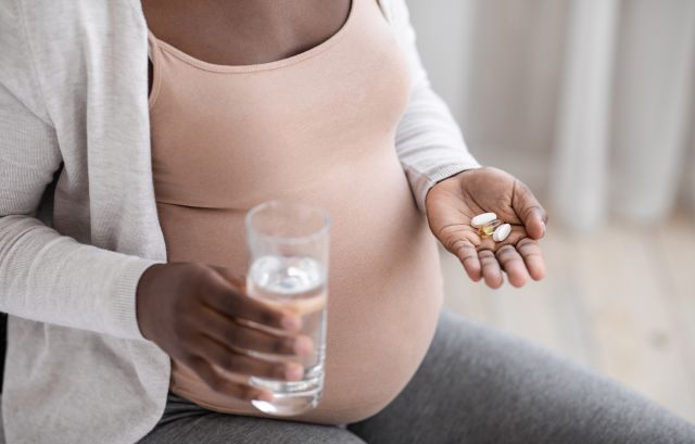 pregnant person holding two pills in one hand and a glass of water in the other hand