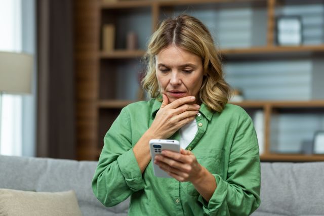 a middle aged white woman looks at a troubling text message she has received from a friend