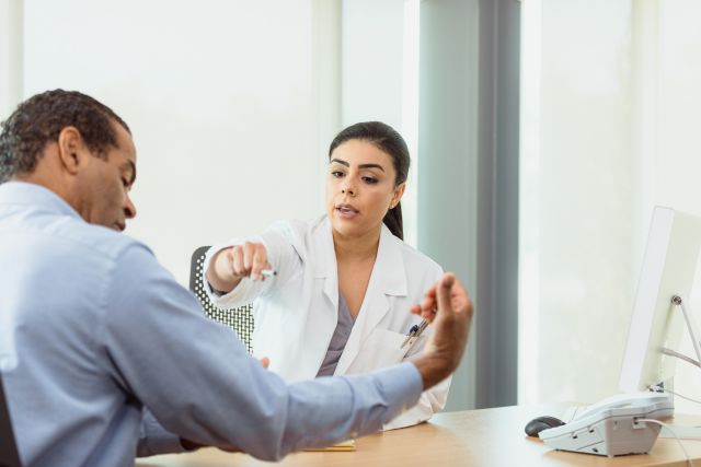 A mid adult female doctor asks a mature male patient questions about the Rheumatoid Arthritis pain in his arm.