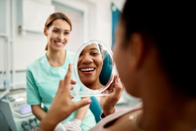 rear view of a happy woman smiling looking at a handheld mirror in a dentist office as a smiling technician looks on