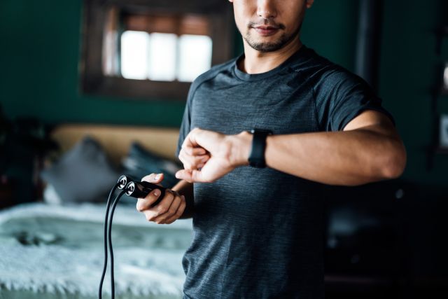 a young, fit Asian American man measures his heart rate after doing a round of jump rope in his bedroom