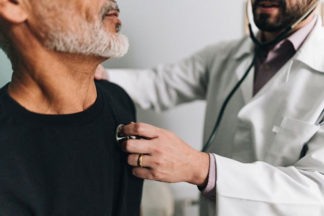 A cardiologist examines an older male patient during an appointment. ATTR amyloidosis can cause problems with the heart as well as the nervous system.