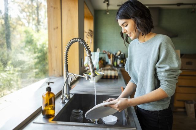 a young women washes dishes smiling