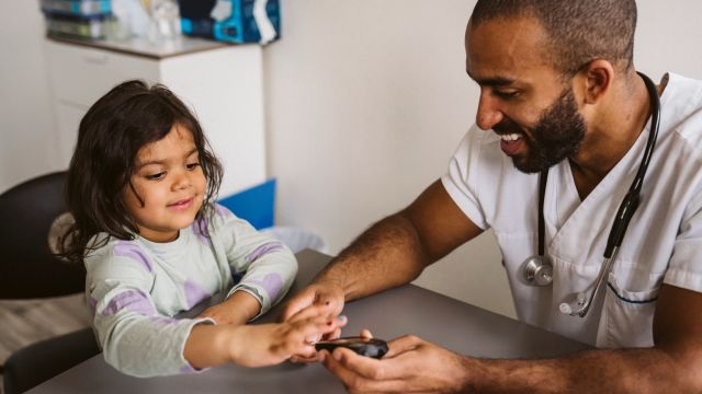 A pediatrician teaches a child how to use a blood glucose meter to check her blood sugar levels.