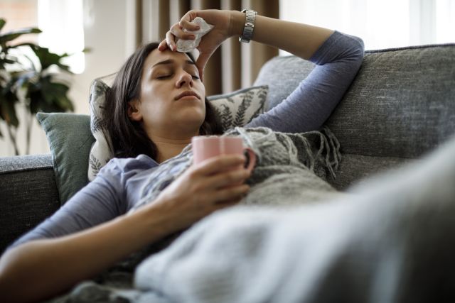 adult woman lies on the sofa sick with the flu holding a cup of tea