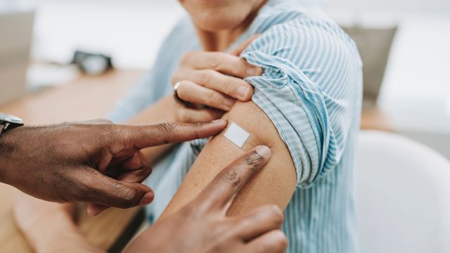 A healthcare provider applies an adhesive bandage to the arm of a senior woman after administering a vaccine.