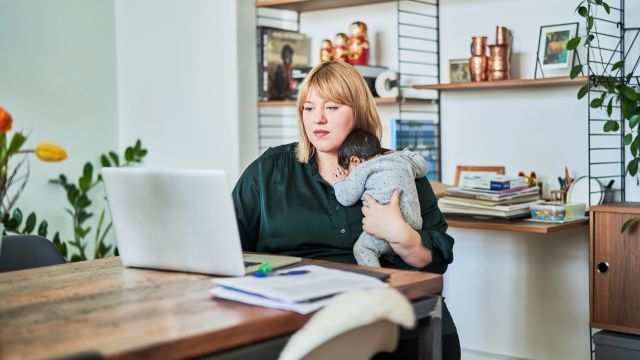 A mom with her young infant child reads about CAH on a laptop computer at home.