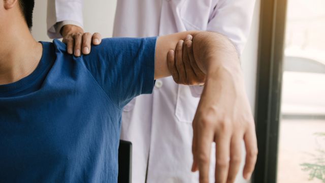 A healthcare provider assesses shoulder pain in a younger male patient during an evaluation for psoriatic arthritis.