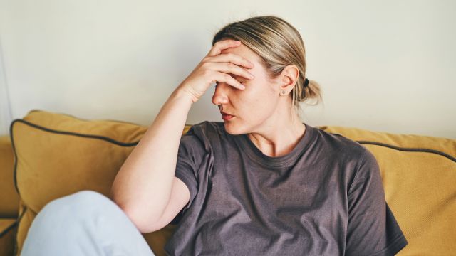 A young woman sits on a couch at home, struggling with low energy and fatigue.