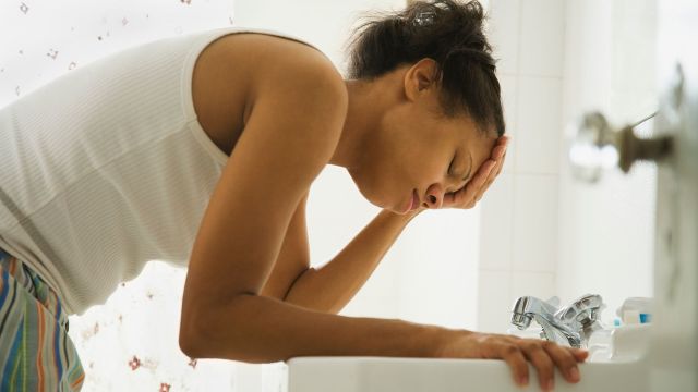 Woman with the stomach flu hovering over a sink nauseous
