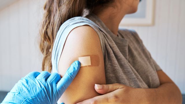 A healthcare provider applies an adhesive bandage to the arm of a young woman who has just received a vaccine. Vaccinations can help prevent infections for people with primary immunodeficiency.