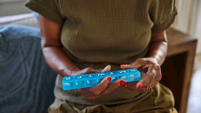 A senior woman uses a pill organizer to keep track of her daily medications. Oral medications called JAK inhibitors are often a part of treatment for myelofibrosis.