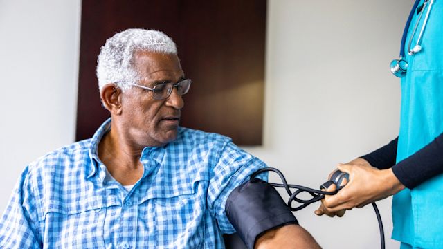 A nurse takes a blood pressure reading for a senior male patient. Elevated blood pressure can contribute to AMD and AMD progression.