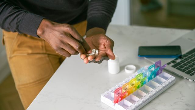 A man organizes his medications into a seven-day pill box. Organization and routine can help a person adhere to treatment with medication.