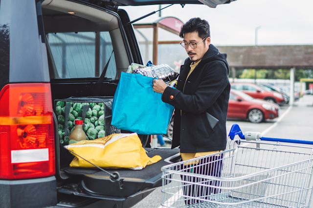 middle-aged Asian man loads groceries into trunk of car