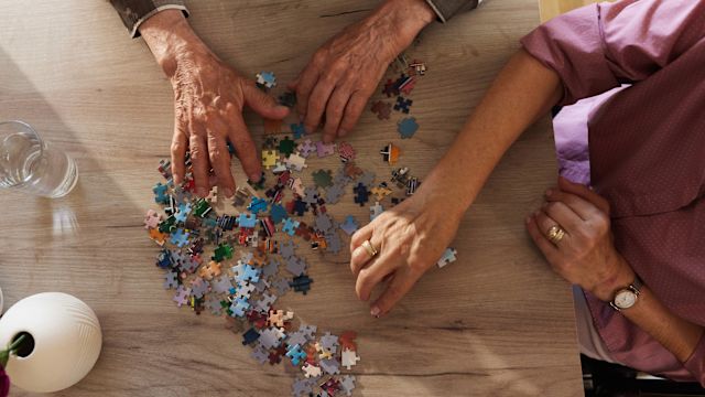 A senior-age man and his adult caregiver work on a jigsaw puzzle. Along with treatment, activities that provide mental stimulation are recommended for people with early-stage Alzheimer's disease.