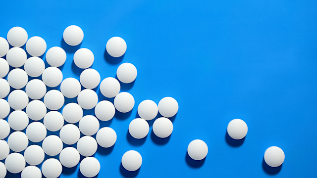 A bottle of pills has been almost emptied onto a black table. There is plenty of copy space available throughout the image.