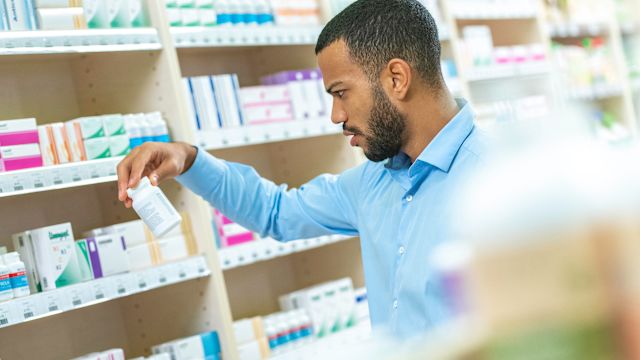 A pharmacist reads the label on a medicine bottle to answer a question for a customer.