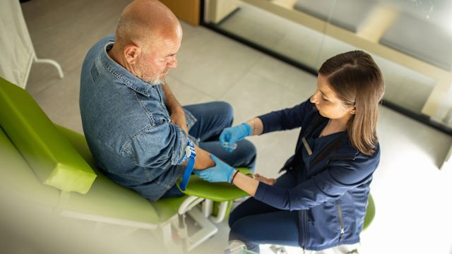 An oncology nurse draws blood from the arm of a middle-aged male patient. Nurses are key members of a multidisciplinary team for metastatic pancreatic cancer.