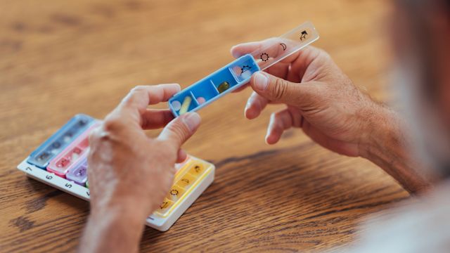 A man takes a dose of medication from a pill organizer. People with MASH may take multiple medications to control blood sugar, cholesterol, blood pressure, and to reduce fibrosis.