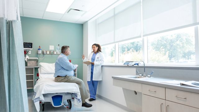 An endocrinologist talks to a middle-aged male patient with hypothalamic obesity in an exam room.