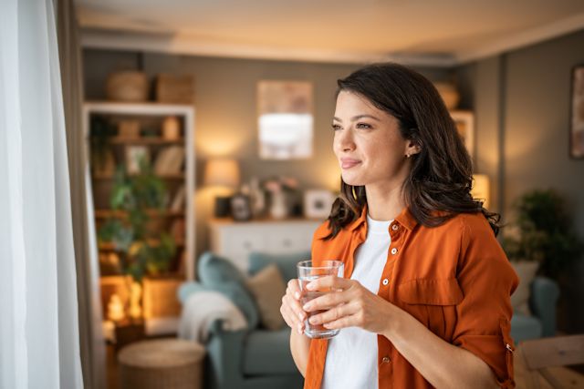 young woman drinking water by window
