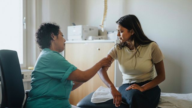 A healthcare provider examines a young woman with ISM at a healthcare office for bone disorders. Osteoporosis is a potential complication of ISM.