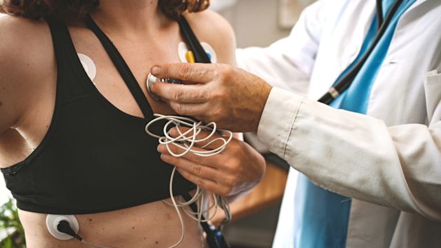 A cardiologist listens to the heartbeat of a female patient wearing a Holter monitor.
