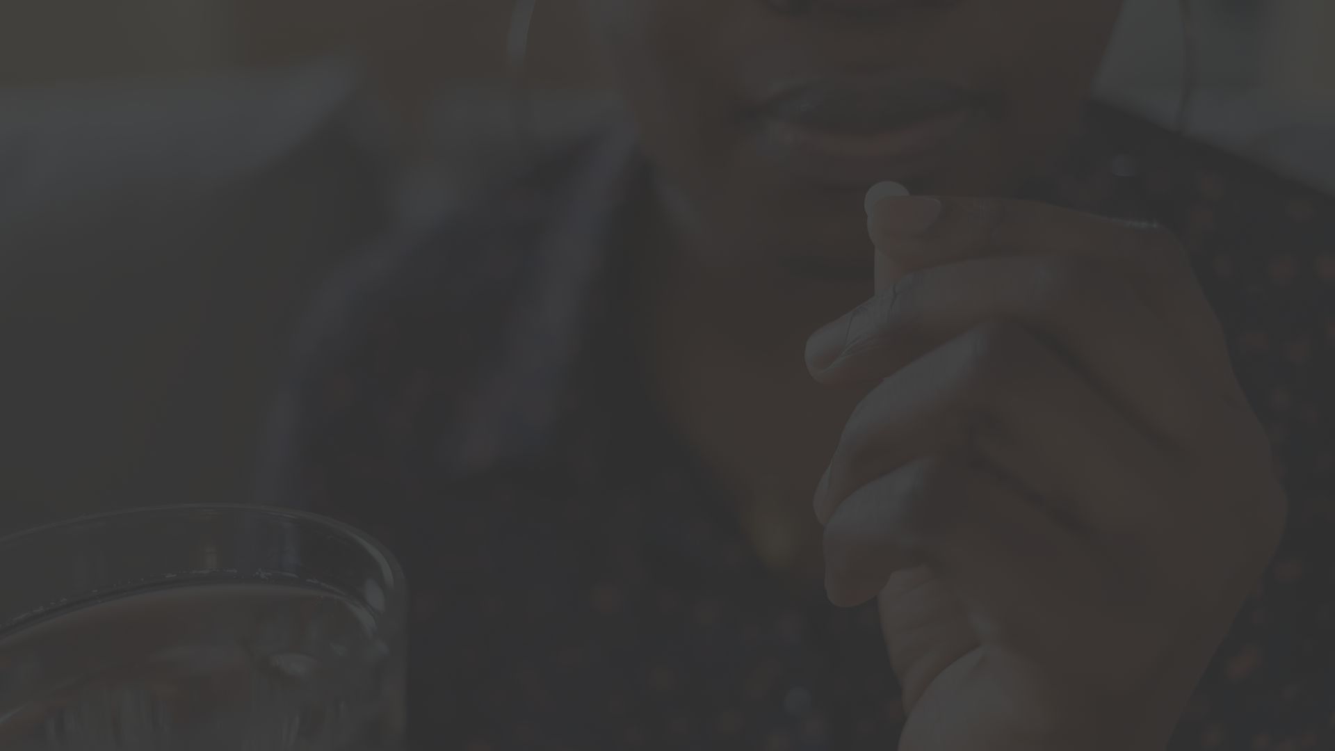 a middle aged Black woman begins to take a pill with a glass of water