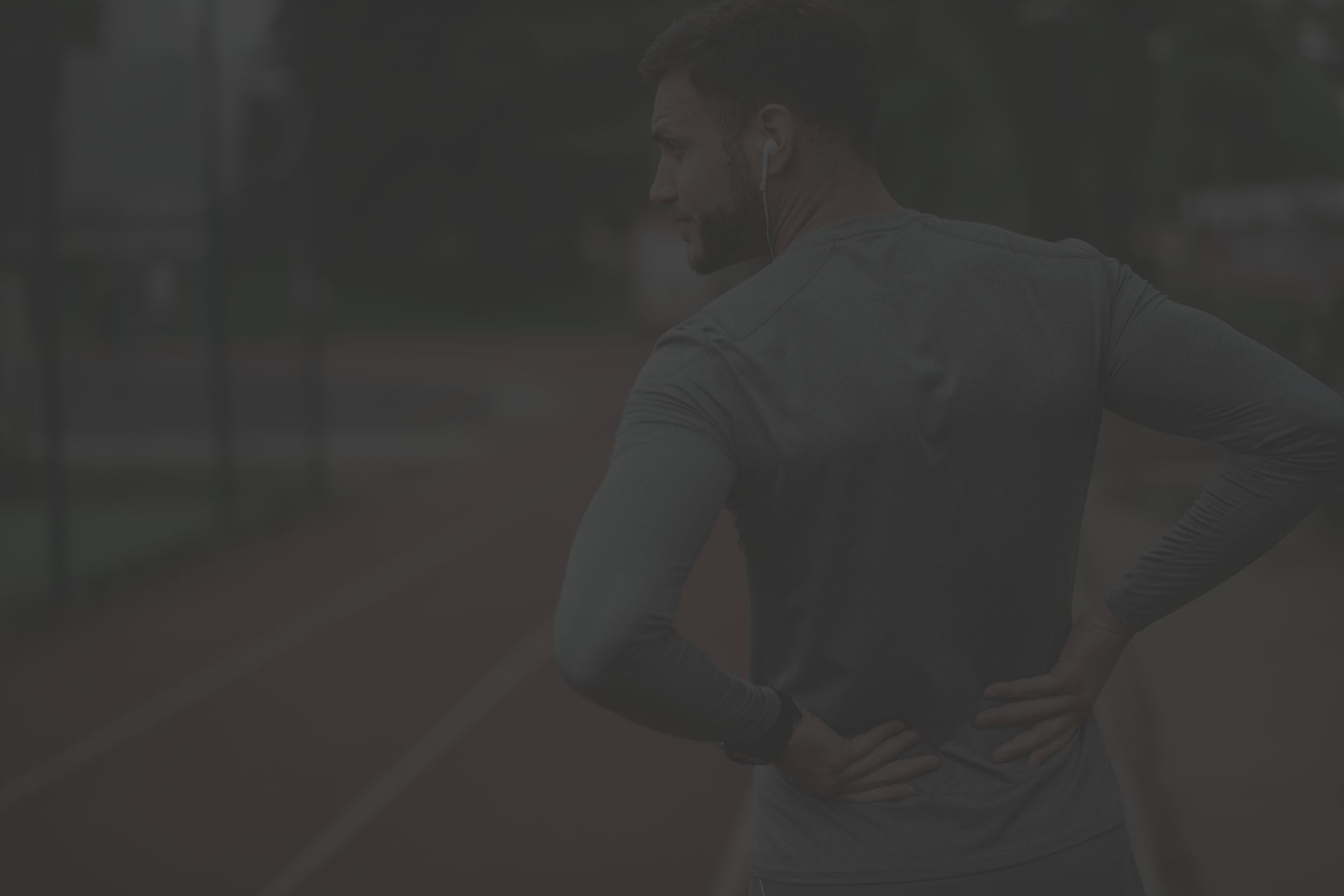 man standing on a running track holding his painful back