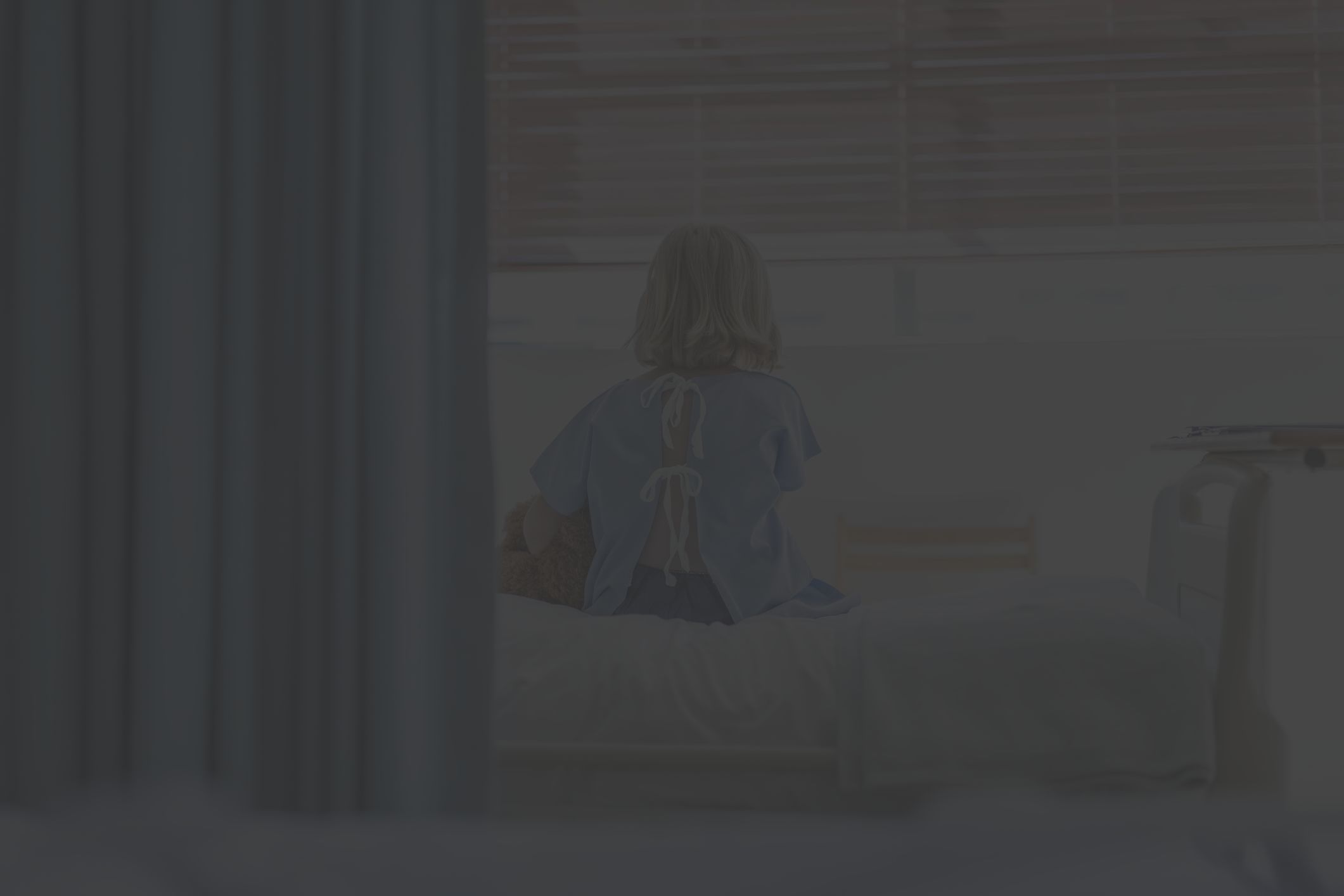 rear view of child with teddy bear on hospital bed